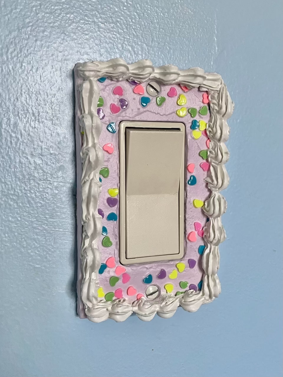 a light switch with a light switch plate decorated to look like a lilac cake with heart shaped sprinkles