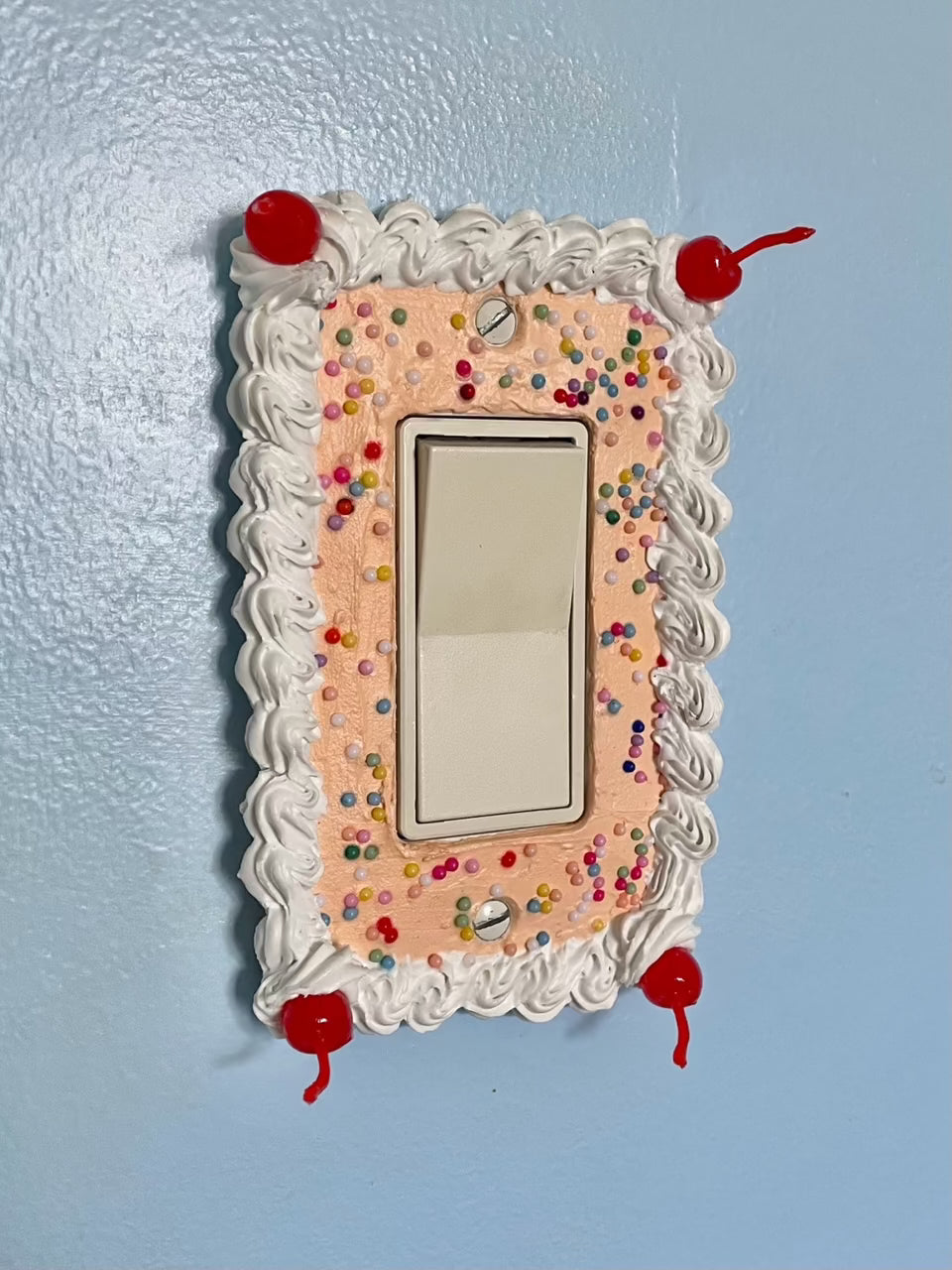a light switch with a light switch plate decorated to look like an orange cake with sprinkles