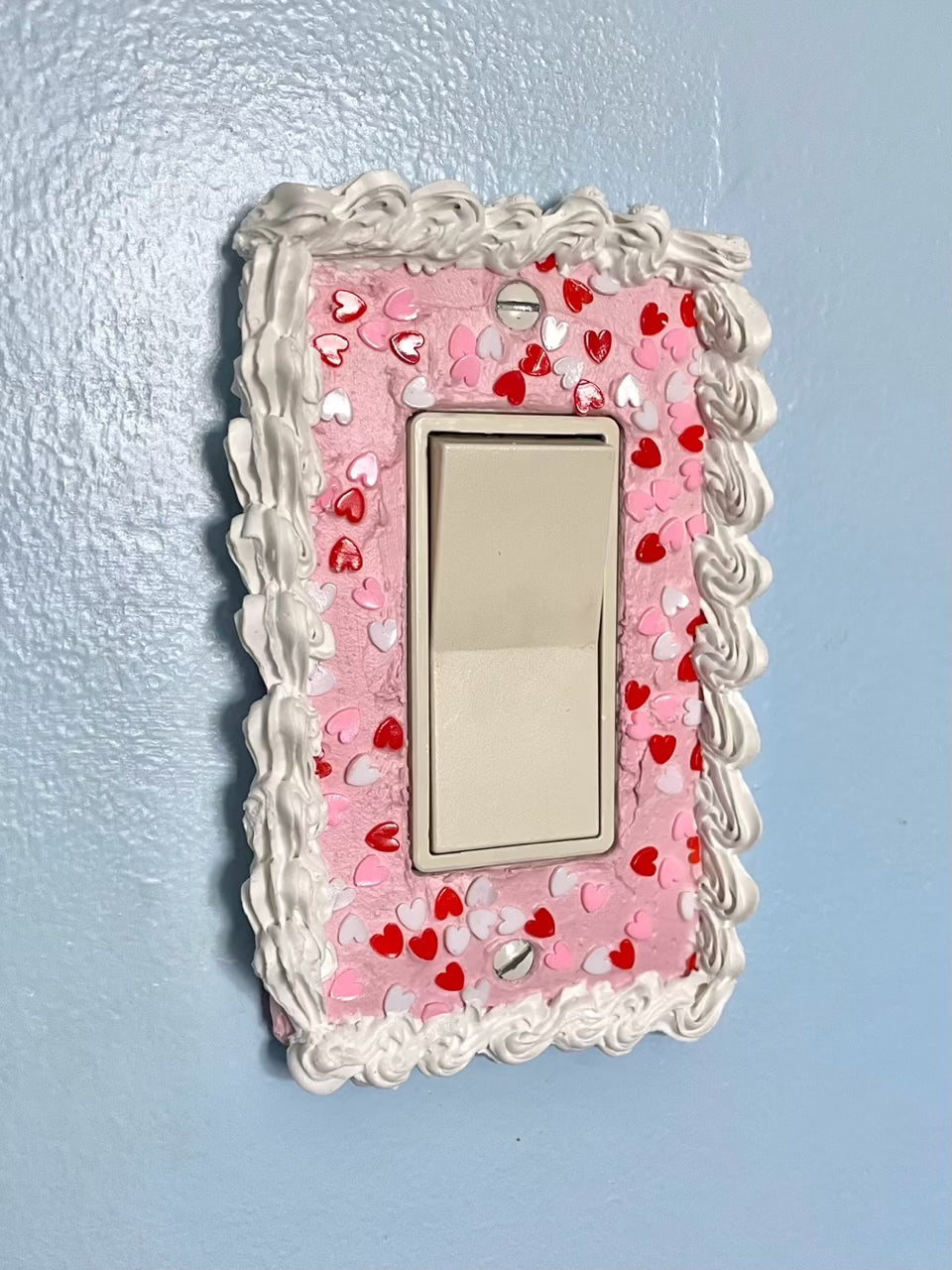 a light switch with a light switch plate decorated to look like a pink cake with heart sprinkles