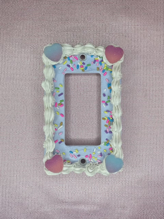 a light switch plate decorated to look like a blue cake with sprinkles and candy hearts