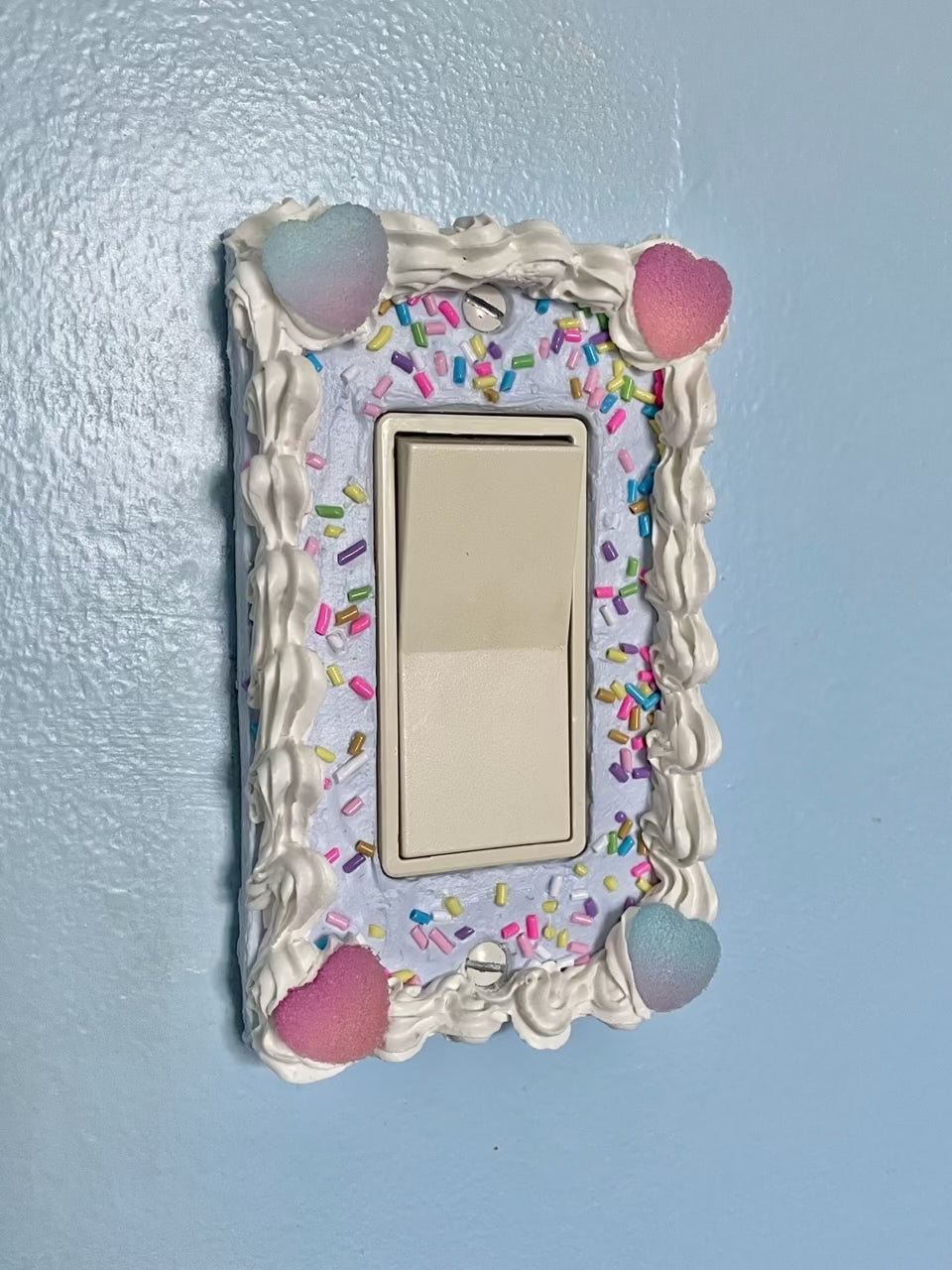 a light switch with a light switch plate decorated to look like a blue cake with sprinkles and candy hearts