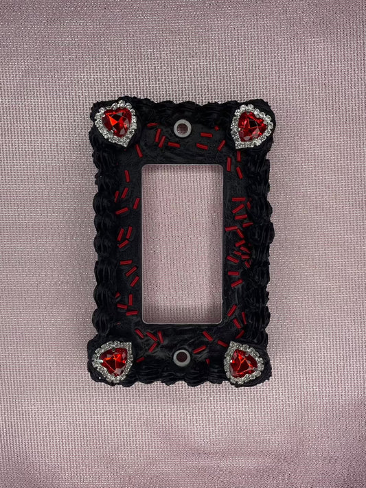a light switch plate decorated to look like a black cake with red sprinkles