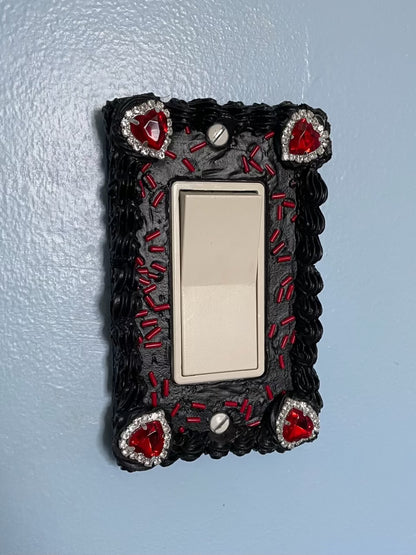 a light switch with a light switch plate decorated to look like a black cake with red sprinkles