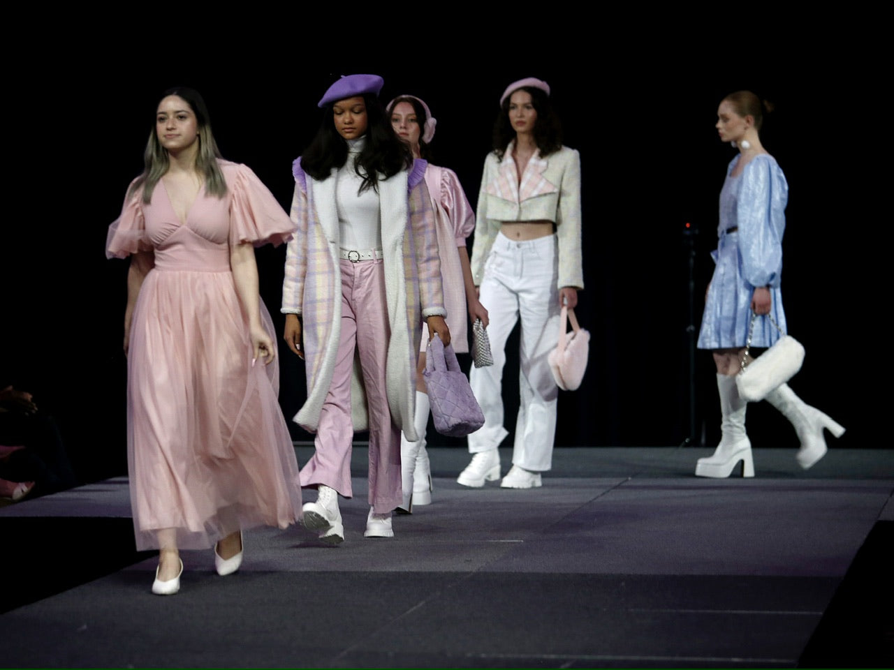 a designer walking down a runway followed by 4 models wearing her pastel wintery designs