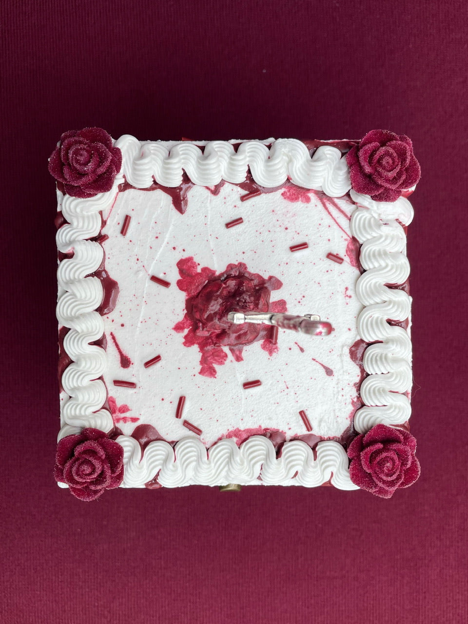 a hinged box decorated to look like a white cake with imitation blood, burgundy sprinkles and a mini sword