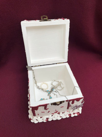 a hinged box decorated to look like a white cake with imitation blood, burgundy sprinkles and a mini sword