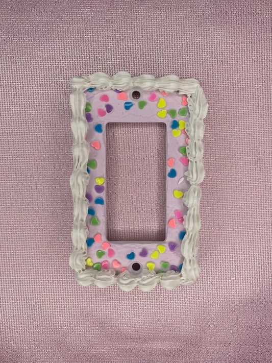 a light switch plate decorated to look like a lilac cake with heart shaped sprinkles