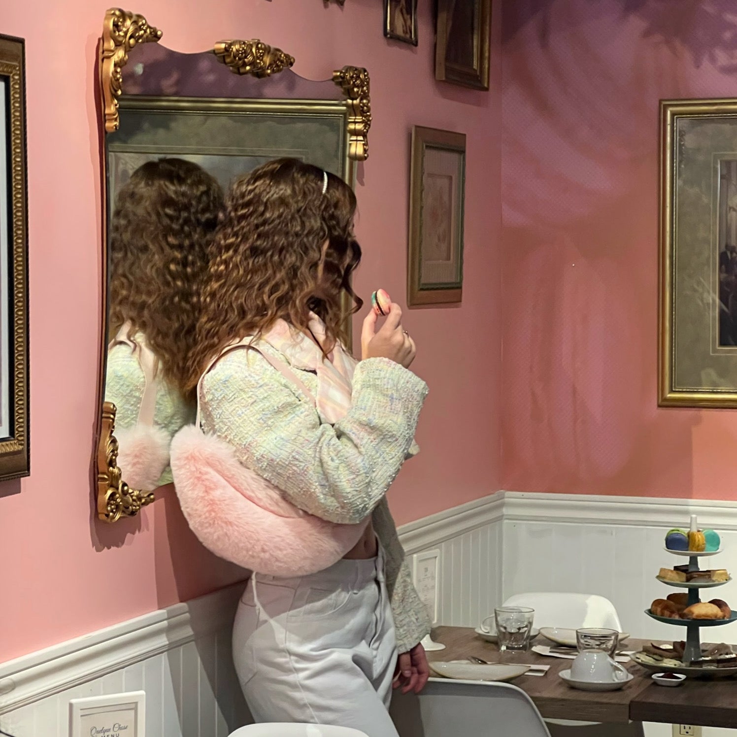 a behind the scenes photo of a women posing in a photoshoot wearing a pastel cropped blazer holding a macaron