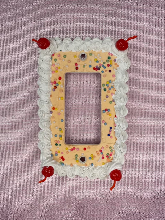 a light switch plate decorated to look like an orange cake with sprinkles