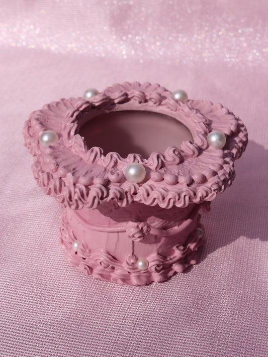a flower shaped candle holder decorated to look like a pink cake with pearl details