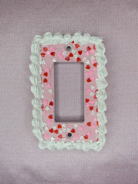 a light switch plate decorated to look like a pink cake with heart sprinkles