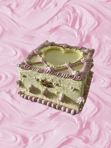 a box decorated to look like a yellow and pink cake on a pink background that looks like icing