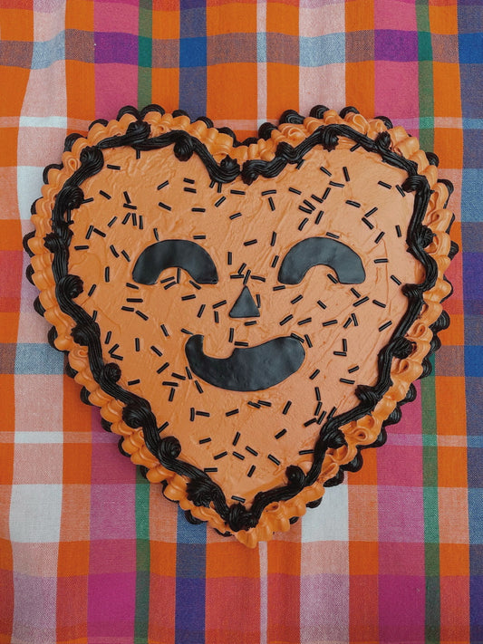 a wall hanging shaped like a heart and decorated to look like an orange and black jack o lantern cake