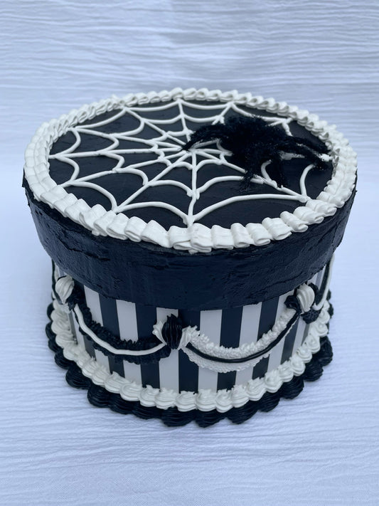 a black and white striped cardboard box decorated to look like a cake with spiderweb icing and a fuzzy spider on top