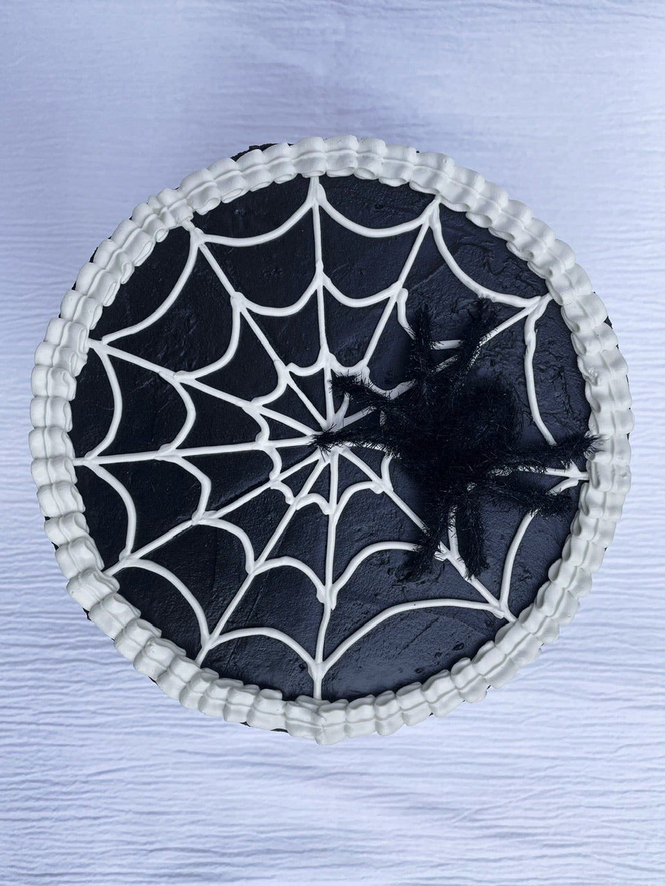 the lid of a black cardboard box decorated with white spiderweb fake icing and a fuzzy spider