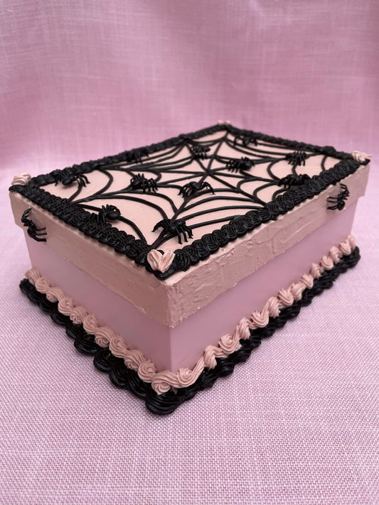 a pink rectangular cardboard box decorated to look like a pink and black cake with tiny plastic spiders on it