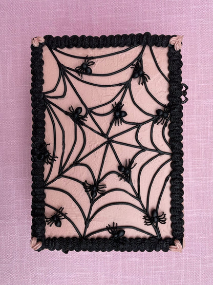 top view of a cardboardbox decorated to look like a pink and black cake with tiny spiders on it